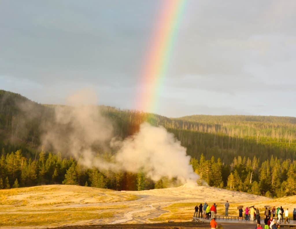 Old Faithful Geyser with a Rainbow. Old Faithful Inn with kids.